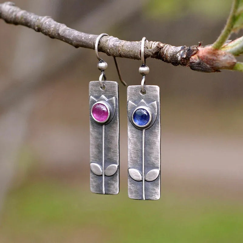 Antique finish red sapphire earrings with geometric shape and elliptical gemstone elements on metal background
