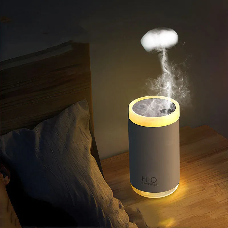 Blue jellyfish-shaped USB humidifier emitting smoke ring mist with warm night light on, placed on a wooden desk.