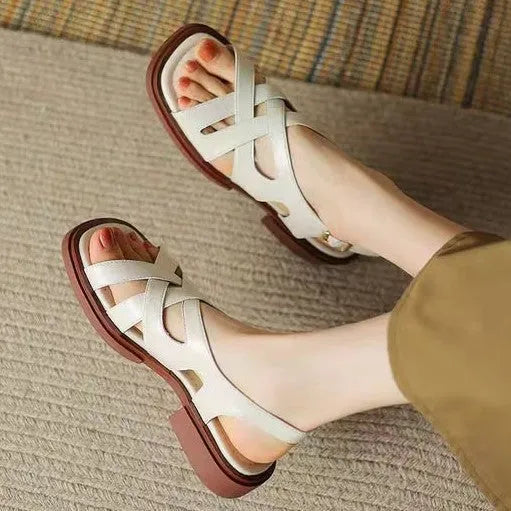 Women's glossy black patent leather sandals with a square toe and a cross-strap design on a low rubber sole.
