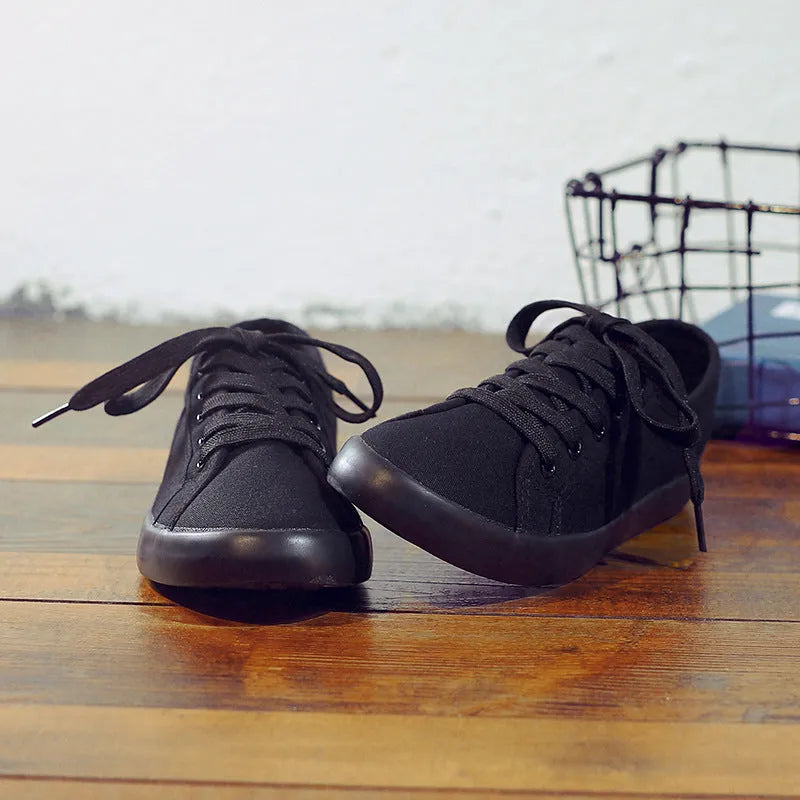All black low top canvas lace-up shoes with a flat rubber sole for women.