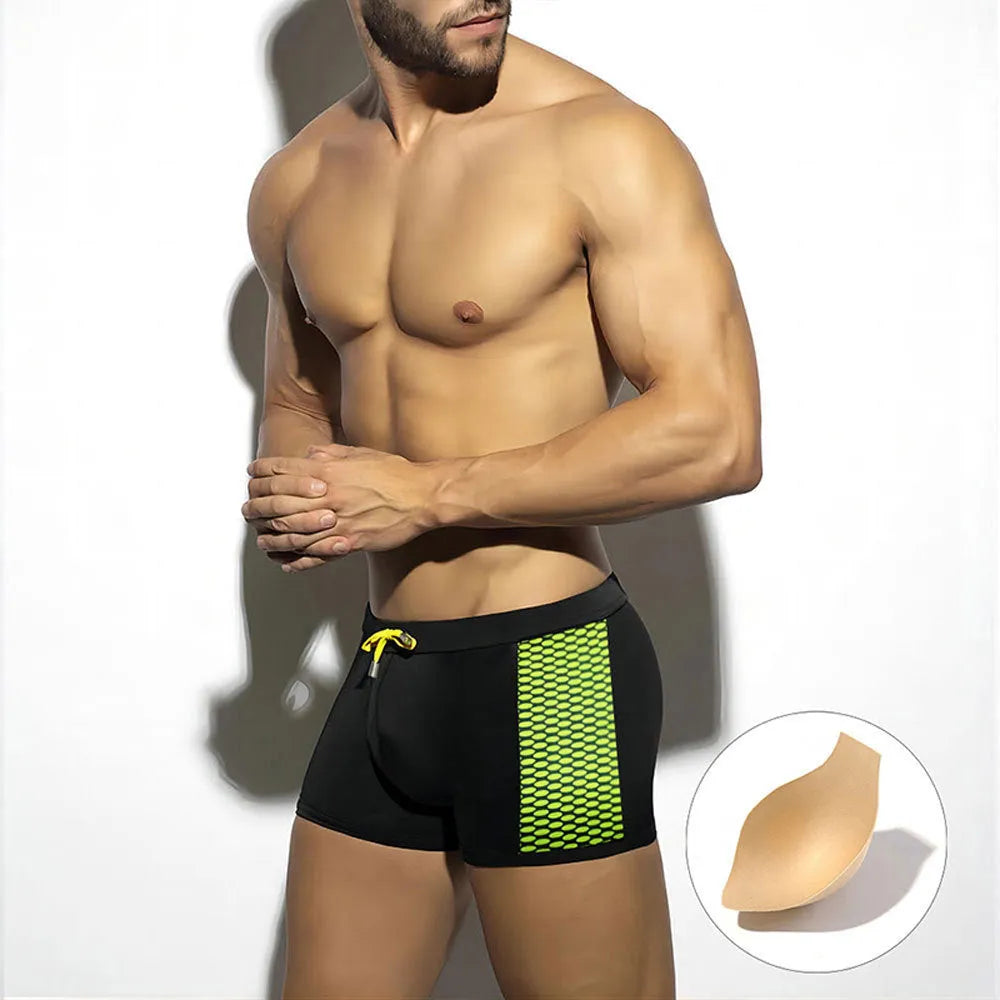 Men's black polka dot swimming boxers with a dark blue ribbon trim on a grey background.