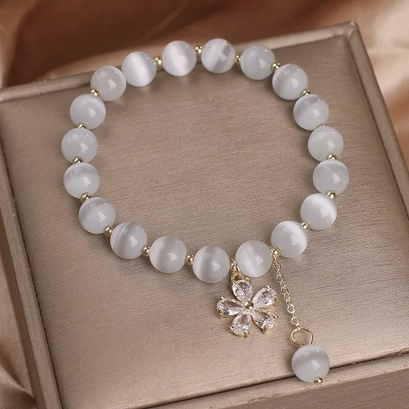 White cat's eye stone bracelet with small flower charms, tassel pendant, and safety buckle clasp.