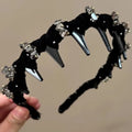 A wine red velvet hairband with a crystal wave decoration, sitting on a dark surface.