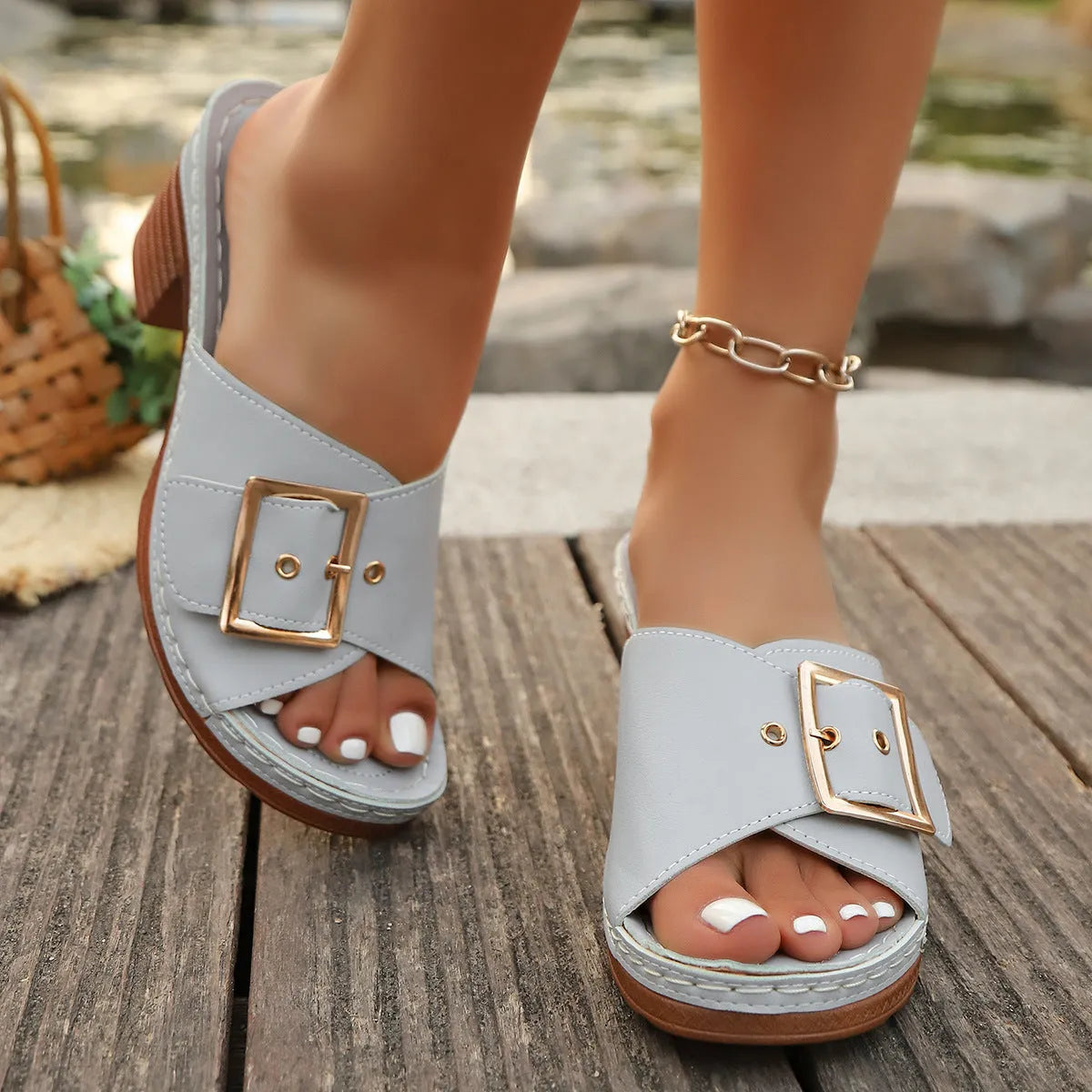 Women's black chunky heel slippers with a round toe and metal buckle detail on a light background.