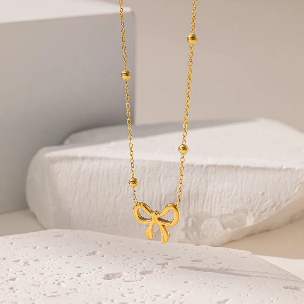Gold electroplated titanium steel bow necklace on a cross chain, adjustable length.