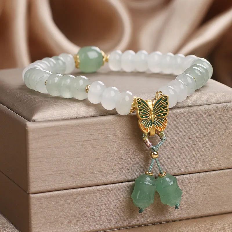 Green crystal abacus bead bracelet with a retro butterfly charm and tassels on a white background.