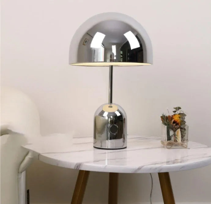 Mushroom-shaped table lamp with a metal base in rose gold finish on a wooden table.