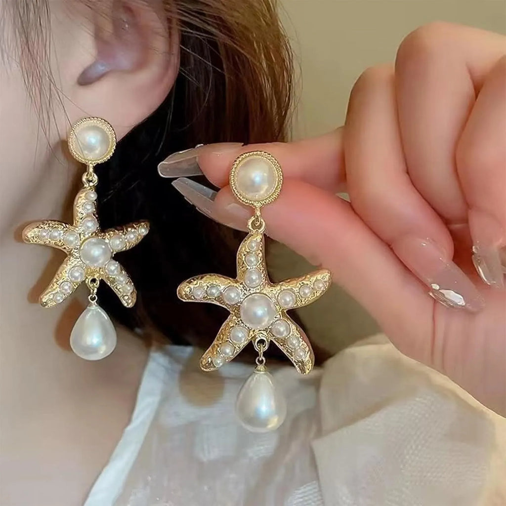 Women's gold-tone starfish drop earrings with a single off-white pearl centre on a light background