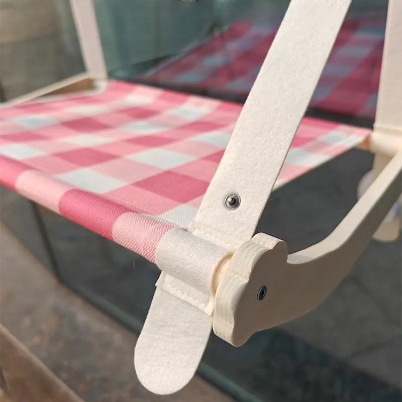 Pink foldable wooden cat window bed with suction cups attached to a glass window
