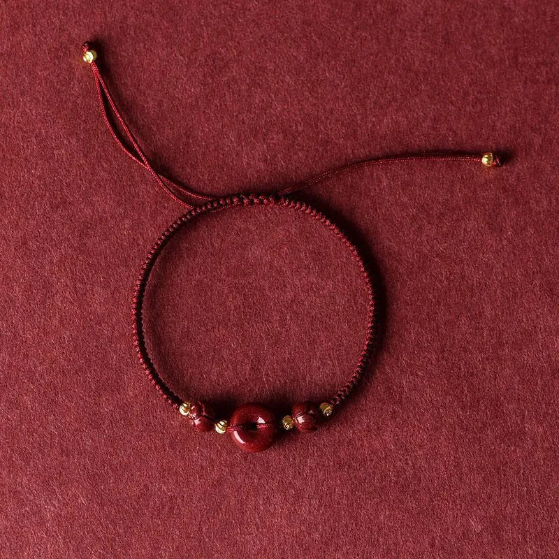 Close-up of a cinnabar heart charm on an adjustable black rope bracelet with a safety buckle.