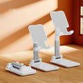 White folding telescopic mobile phone bracket holding a smartphone on a desktop