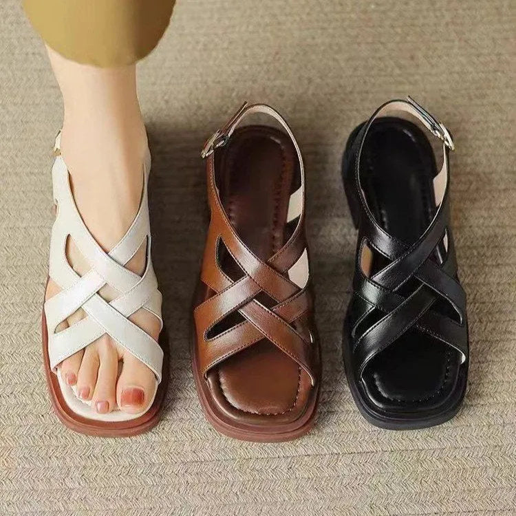 Women's glossy black patent leather sandals with a square toe and a cross-strap design on a low rubber sole.