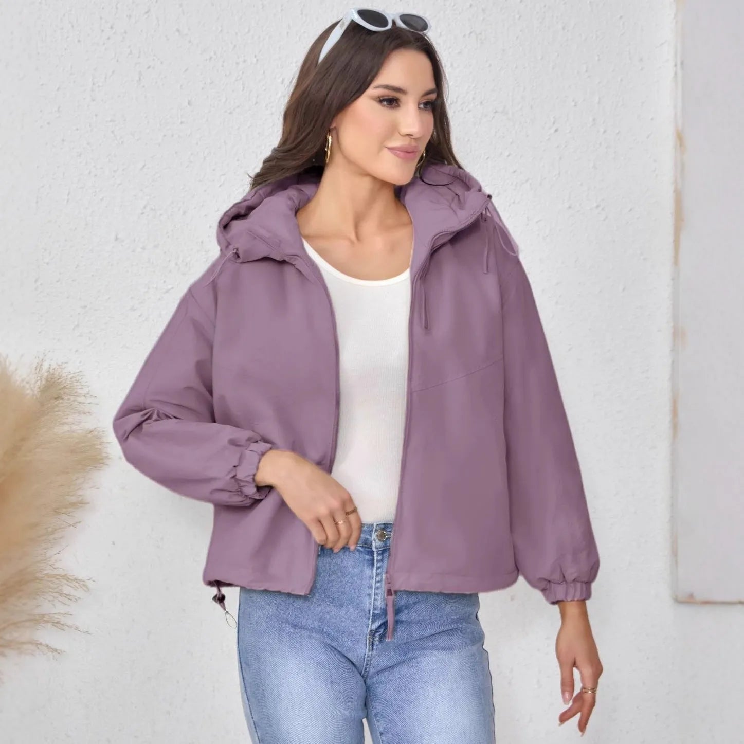 A woman wearing a loose-fitting grey hooded shell jacket with long sleeves, showing the front zip closure.