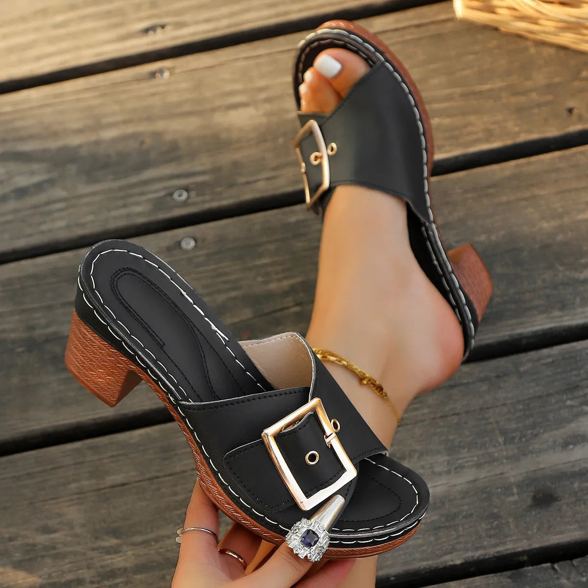 Women's black chunky heel slippers with a round toe and metal buckle detail on a light background.
