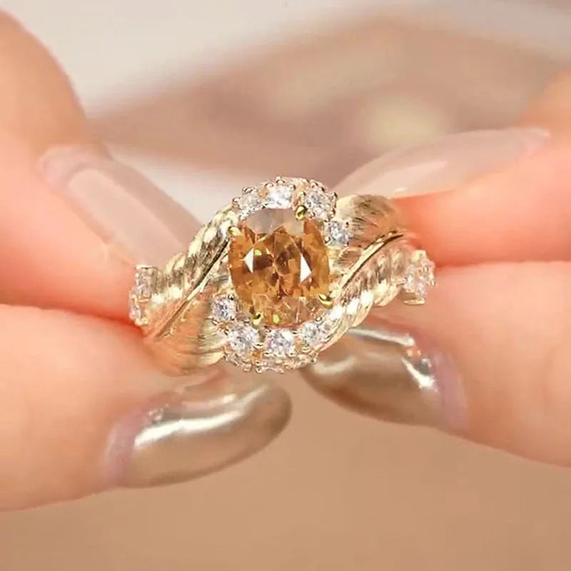 Gold women's ring with embossed feather pattern and a yellow zircon stone on a geometric copper band.